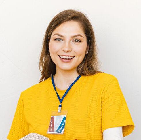 Cheerful young woman in yellow shirt holding a donation box with clothes against a white background.